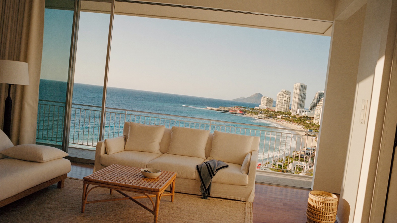 A furnished Waikiki condominium living room opening onto a lanai, looking out over the Pacific, the Waikiki shoreline and Diamond Head.