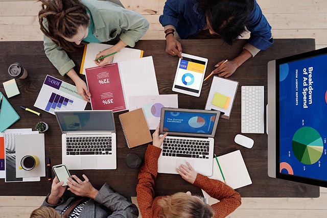 group-working-at-table-with-laptops-tablets-and-marketing-charts