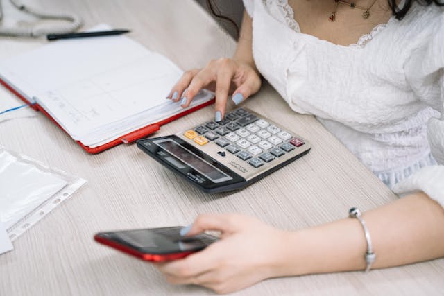 A person running numbers on a calculator beside paperwork.