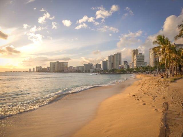 The Honolulu shoreline and skyline at sunset, seen along the beach.