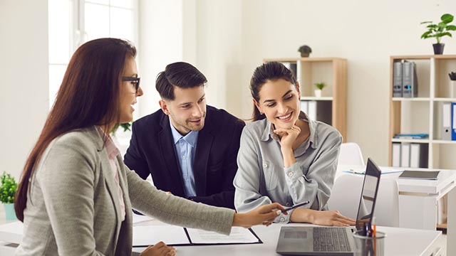 An adviser presenting figures on a laptop to a couple in an office.