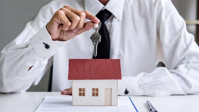 A hand holding a set of keys above a small model house.