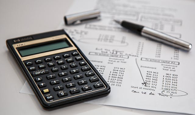A calculator resting on paperwork beside a pen.
