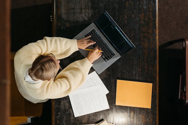 A person working at a laptop beside paperwork.