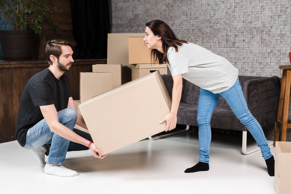 Two people carrying moving boxes out of a property.
