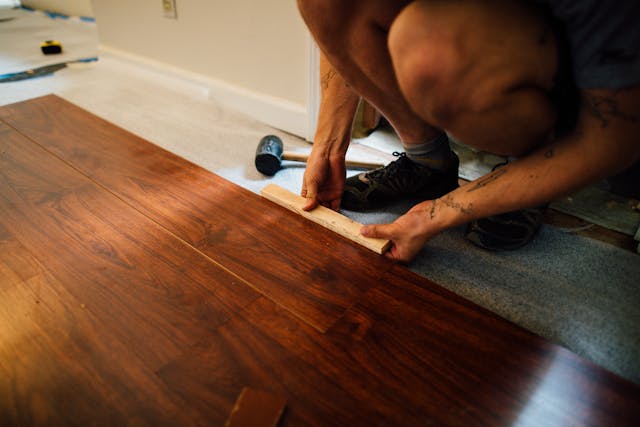 A person kneeling while installing brown plank flooring.