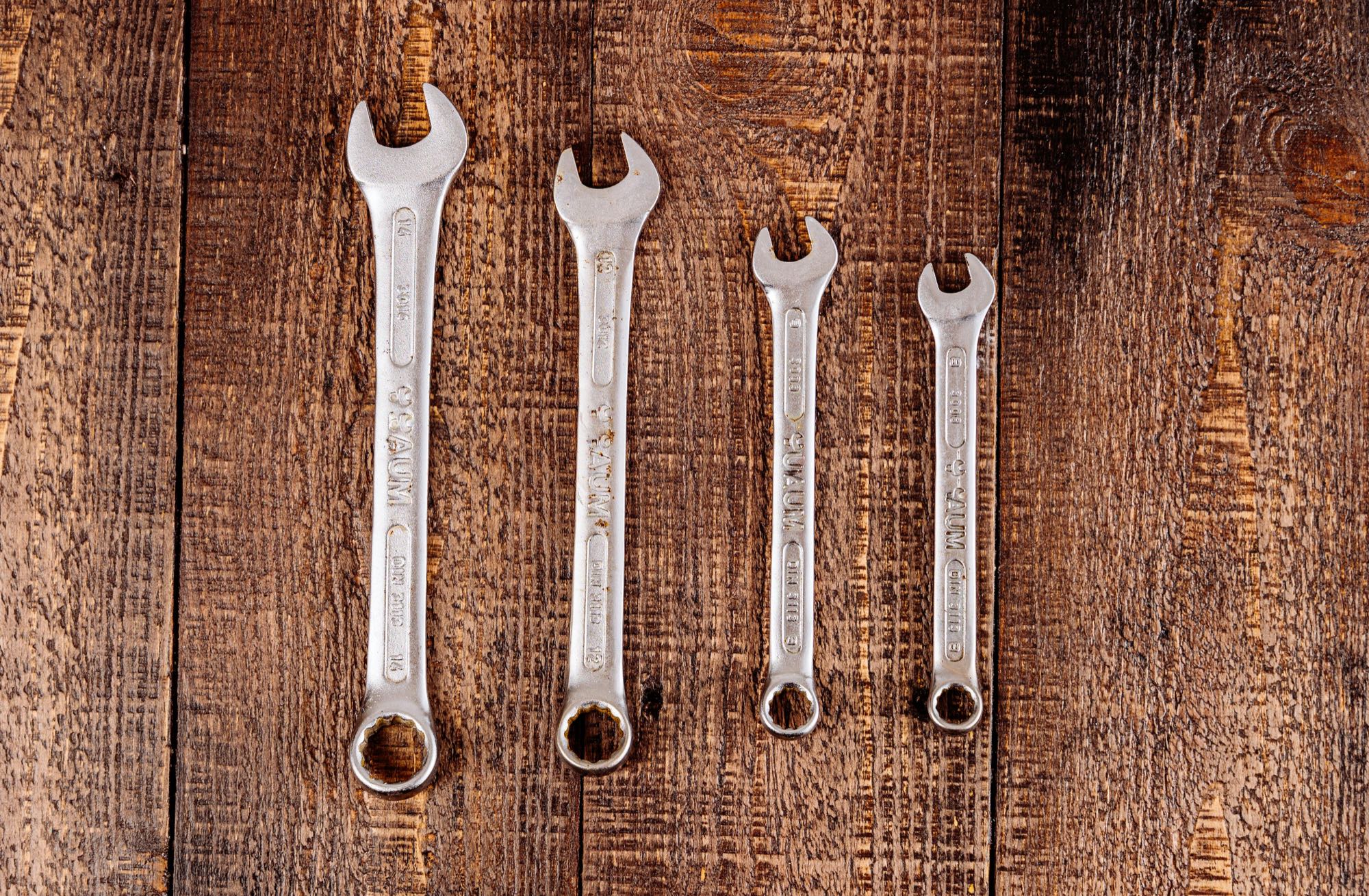 A set of wrenches laid out in a row on a dark wooden workbench.