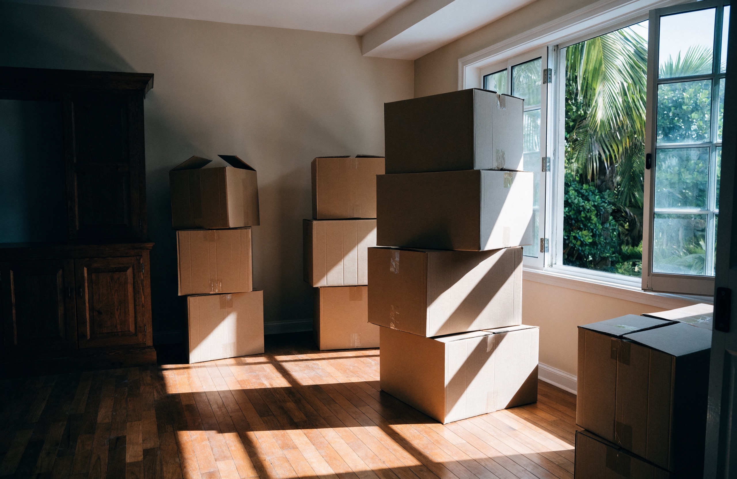 Packed cardboard moving boxes stacked in the sunlit living room of a Hawaii home during a move.
