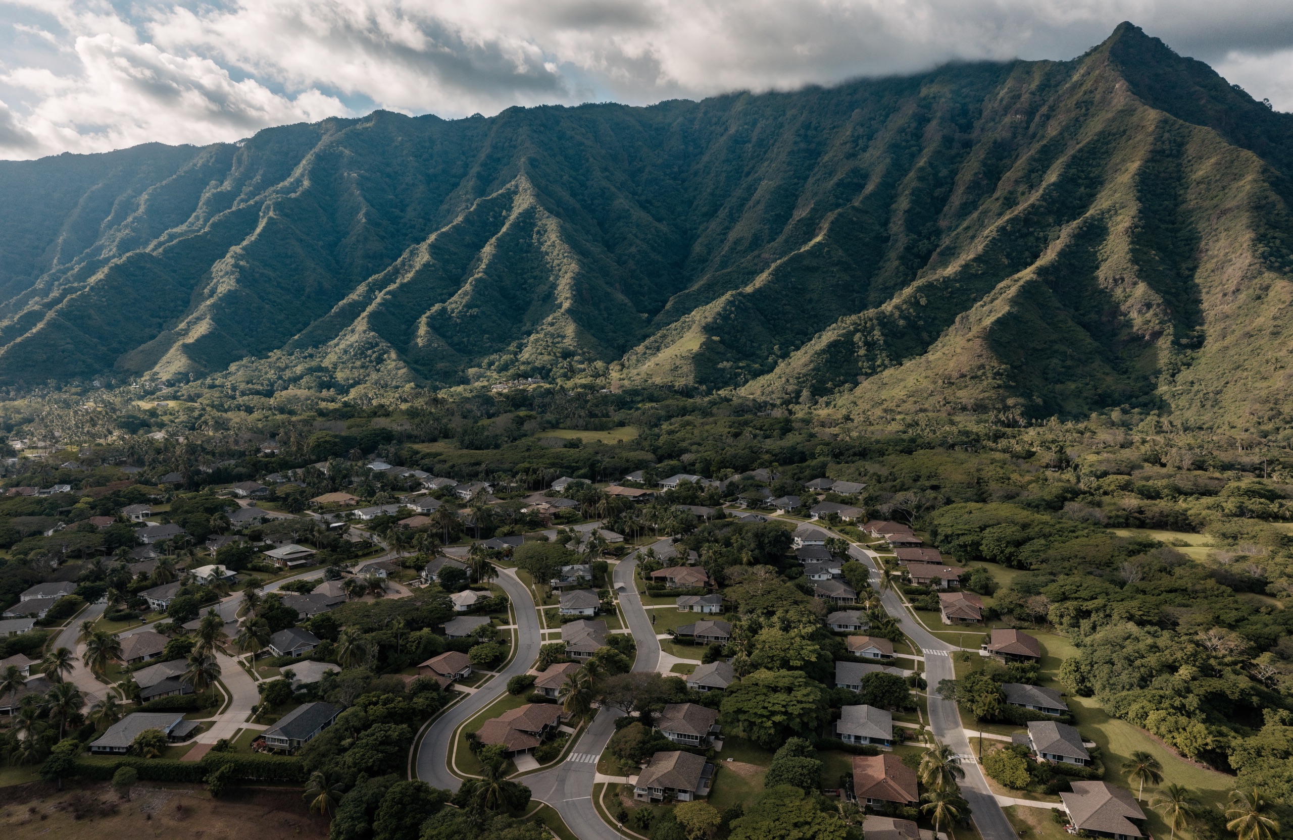 Aerial view of an Oahu residential neighborhood of single-family homes below the green Koolau mountain ridgeline.
