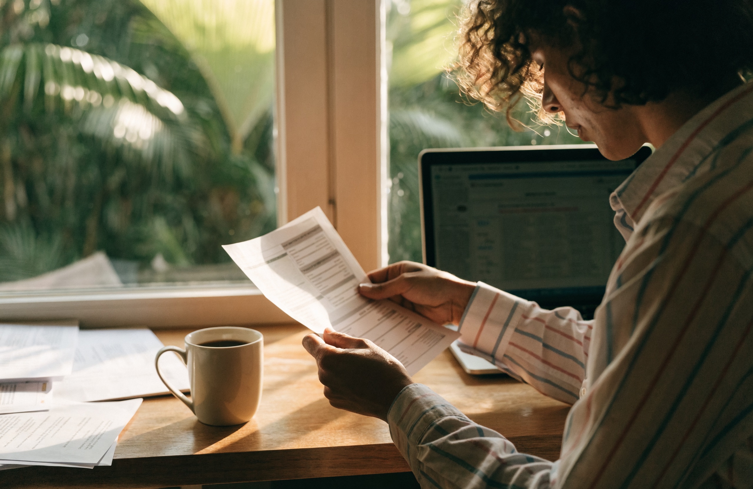 A rental property owner reviewing a printed owner statement at a desk beside a laptop.