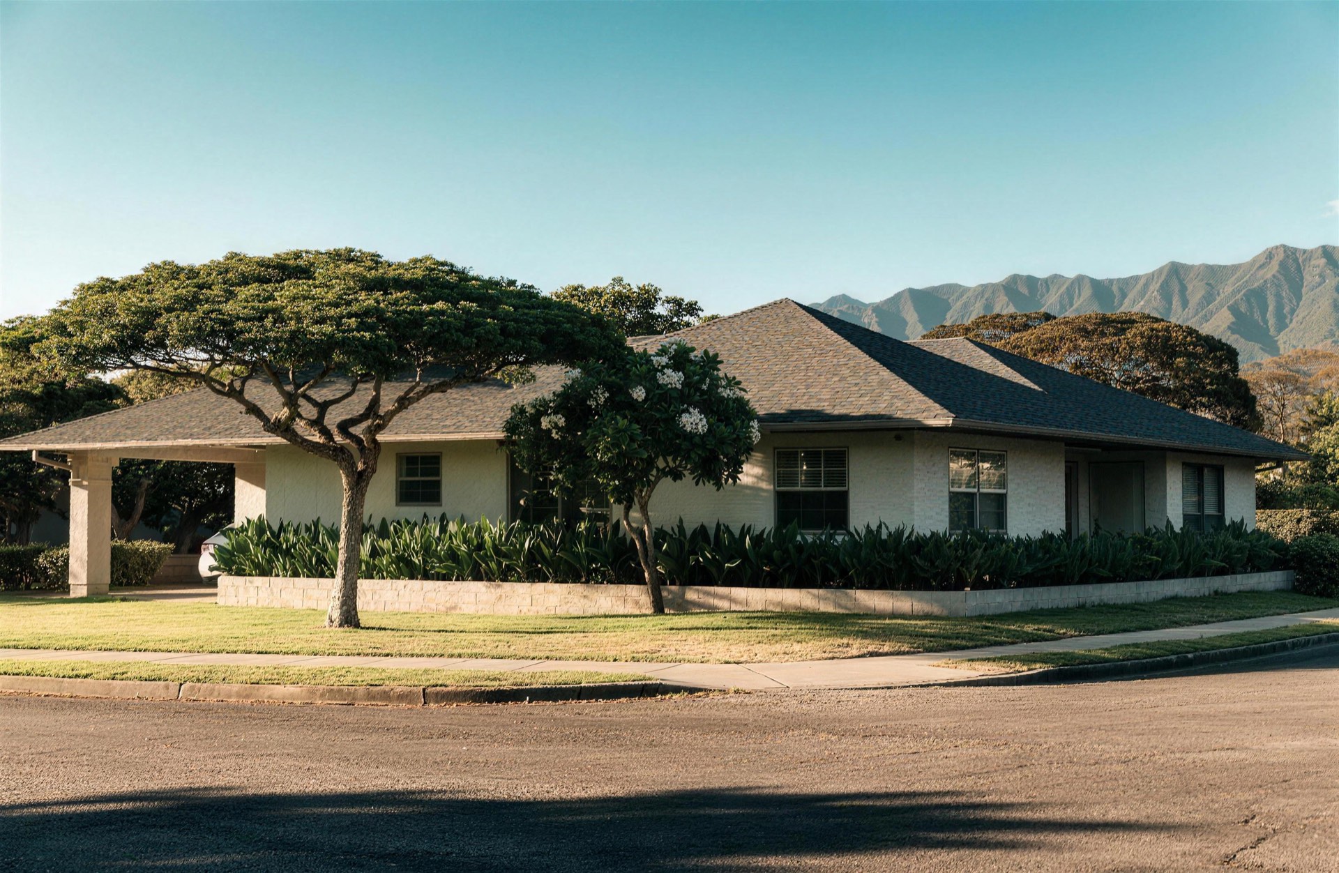 Single-story home with a carport and low garden wall on a tree-lined street in an established Honolulu neighborhood, with a green ridgeline behind it.